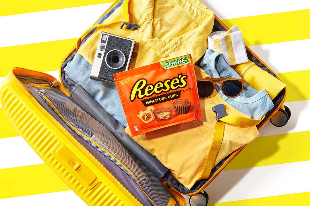 suitcase filled with clothing, accessories, and bag of reeses miniatures peanut butter cups